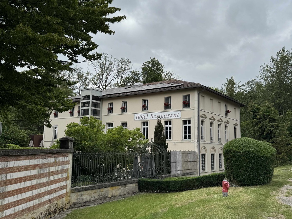 Le Clos de Mutigny seen from the front: a cream-painted bourgeois residence with Hôtel Restaurant lettering above the windows, set behind a hedge and railings under a grey sky